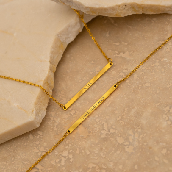 Graveerbare minimalistische bar armband in de kleur goud op een stenen achtergrond