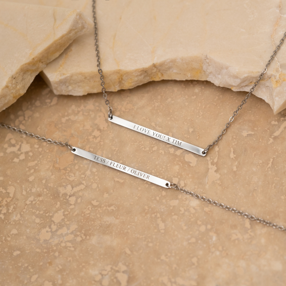 Graveerbare minimalistische bar armband in de kleur zilver op een stenen achtergrond