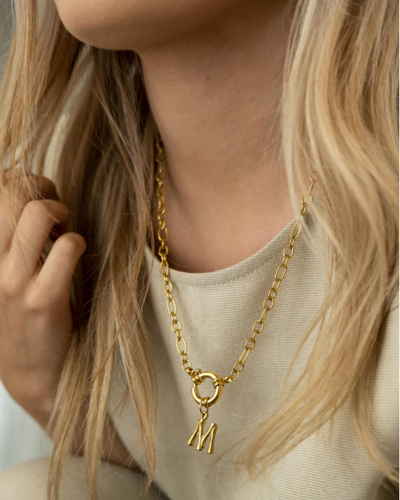 Het model draagt de mooie ketting met kapittelslot met letter in het goud om haar hals