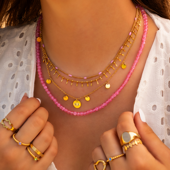 Model draagt necklace layer met mooie gouden en roze kettingen