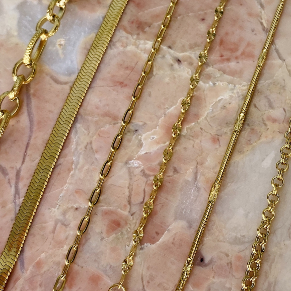 Gouden sieraden met schakels gemixt op roze marmer