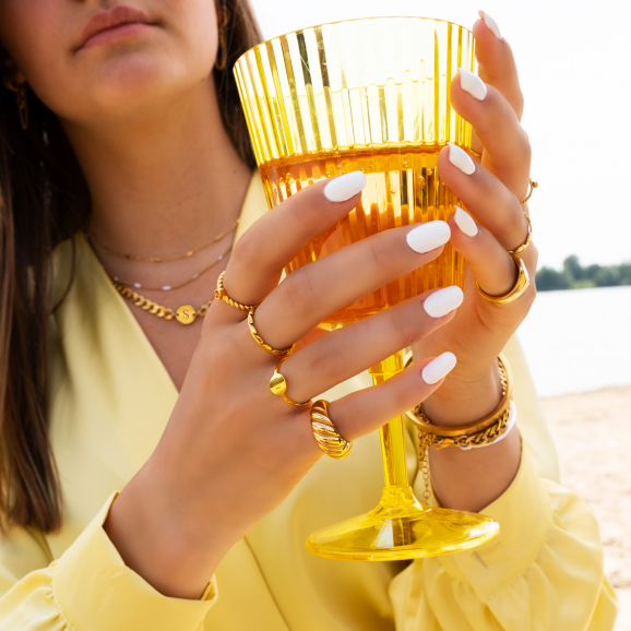 Vrouw met drankje op strand draagt gouden ringen