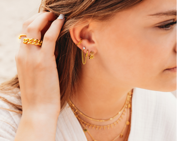 Model draagt gouden sieraden look met oorbellen ringen en kettingen