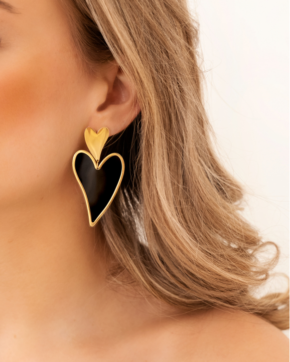 Model draagt gouden en zwarte hartjes oorbellen
