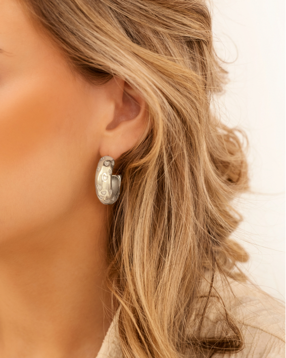 Model draagt zilveren oorbellen met uitgesneden hartjes