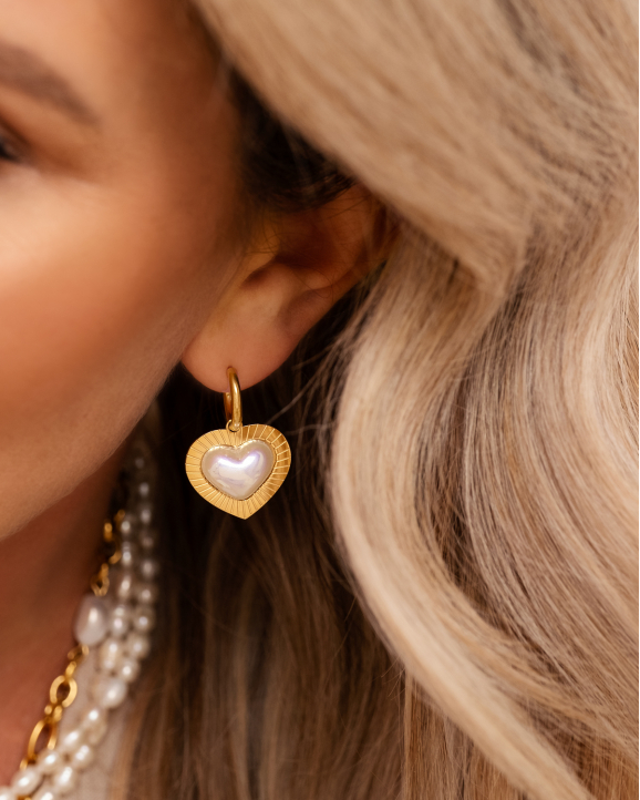 Model draagt gouden hartjes oorbellen met parel