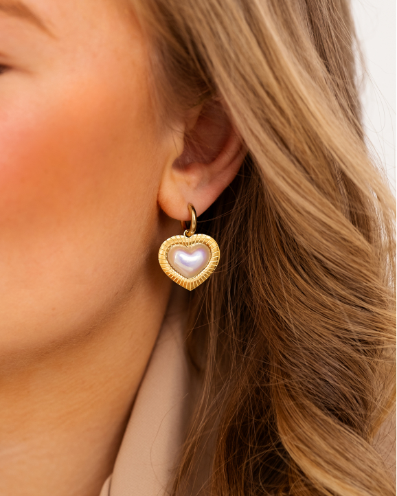 Model draagt gouden hartjes oorbellen in oor