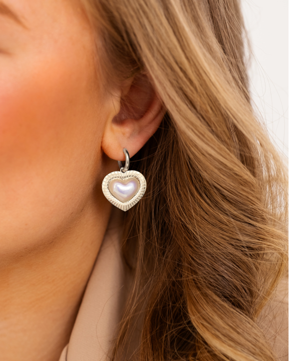 Model draagt zilveren hartjes oorbellen met parel