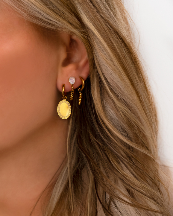 Model draagt gouden oorbellen met vintage coin