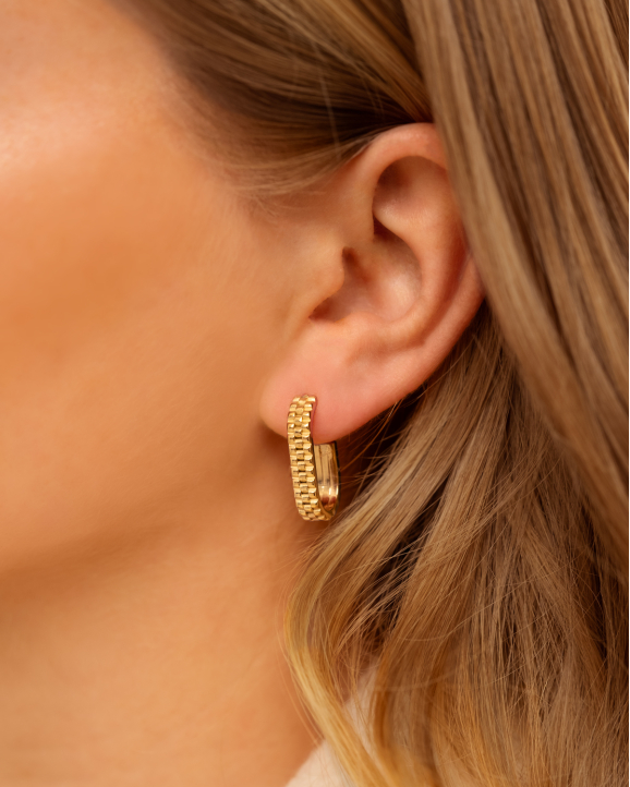 Model draagt gouden oorbellen met print in oor