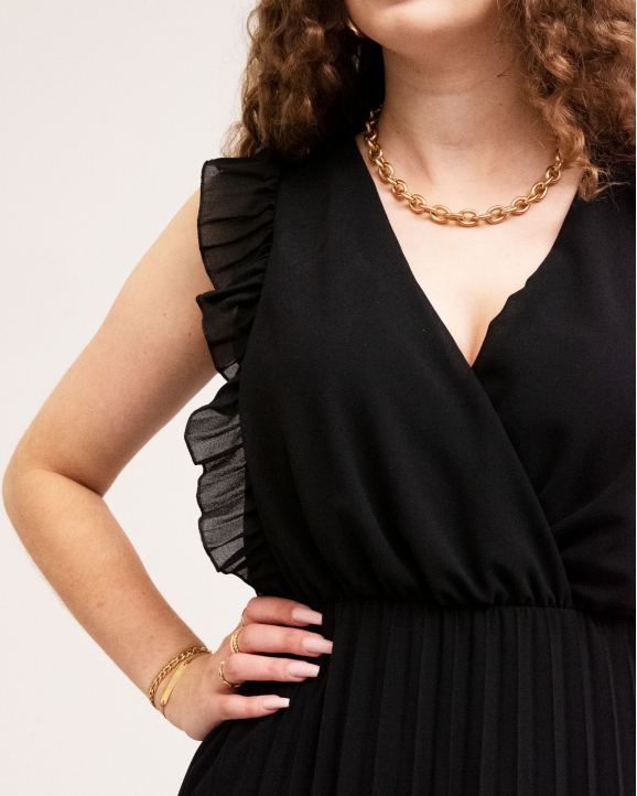 Details van de zwarte plissé jurk met als detail de ketting