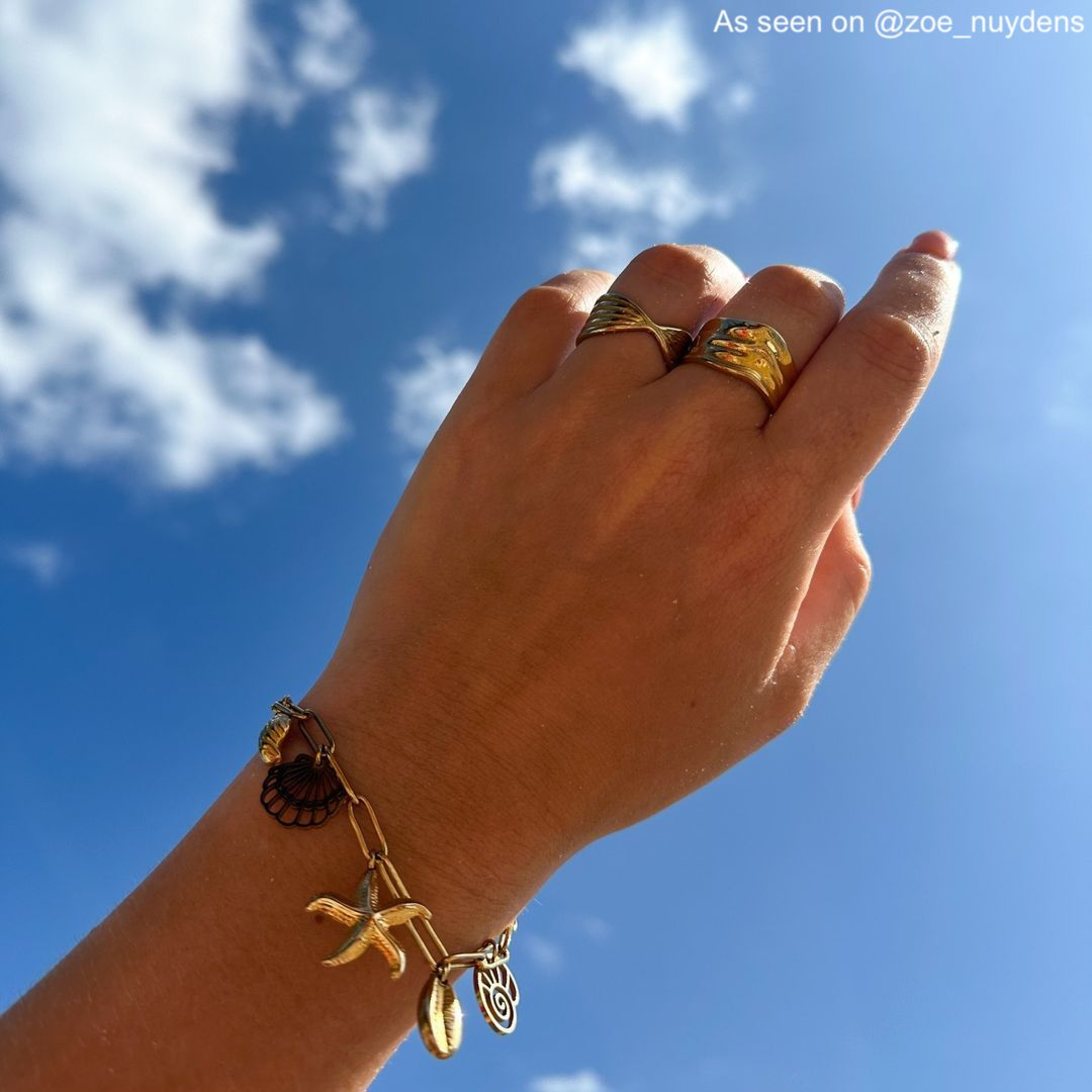 Gouden ringen en bedelarmband bij blauwe lucht