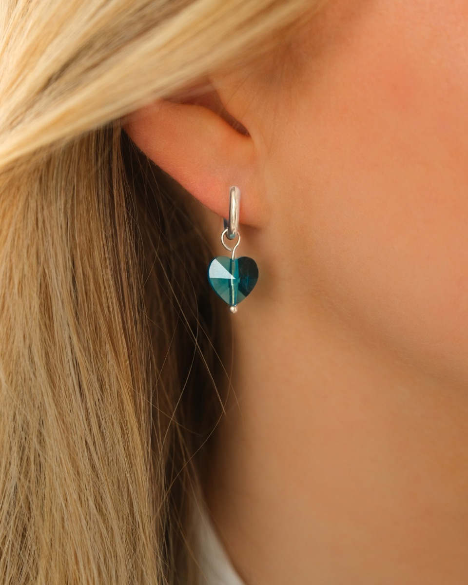 Model draagt zilveren oorringetje met blauw hartje