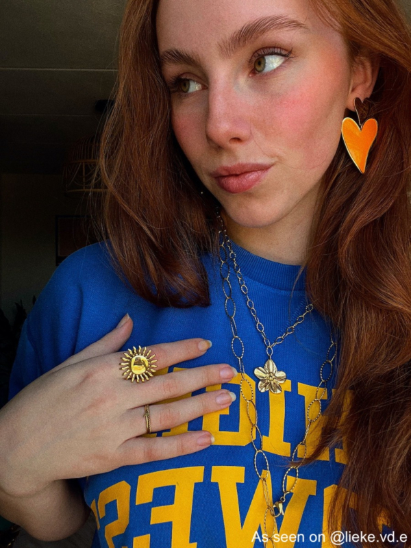 Influencer met oranje oorbellen, 2 gouden kettingen en 2 ringen