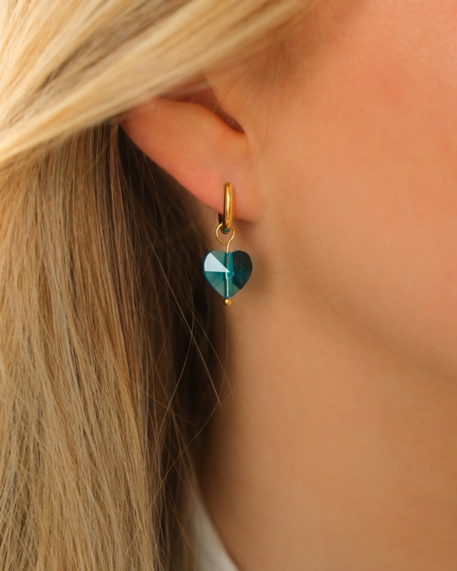 Model draagt gouden oorringetje met blauw hartje