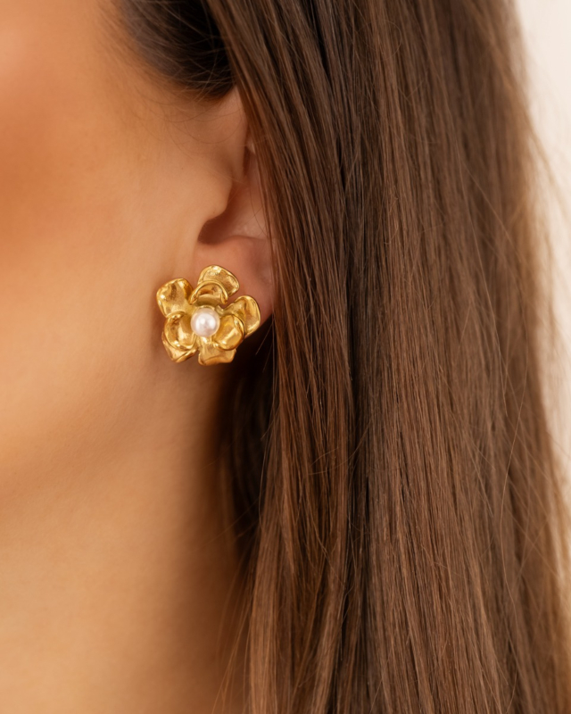Model draagt gouden bloemetjes studs met pareltje