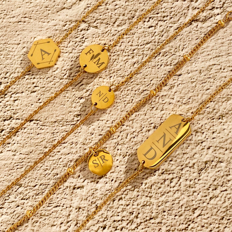 Gouden armbandjes met naam en letters op stenen ondergrond