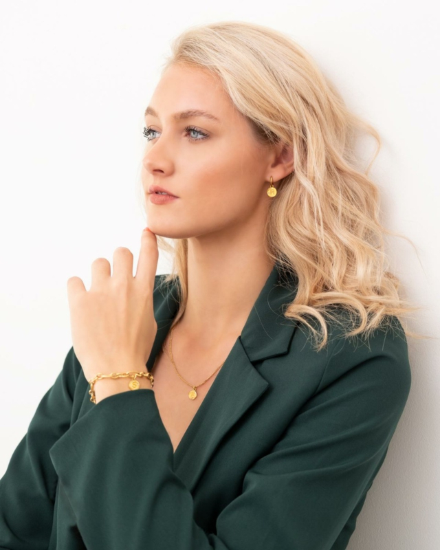 Model draagt gouden sieraden met initiaal