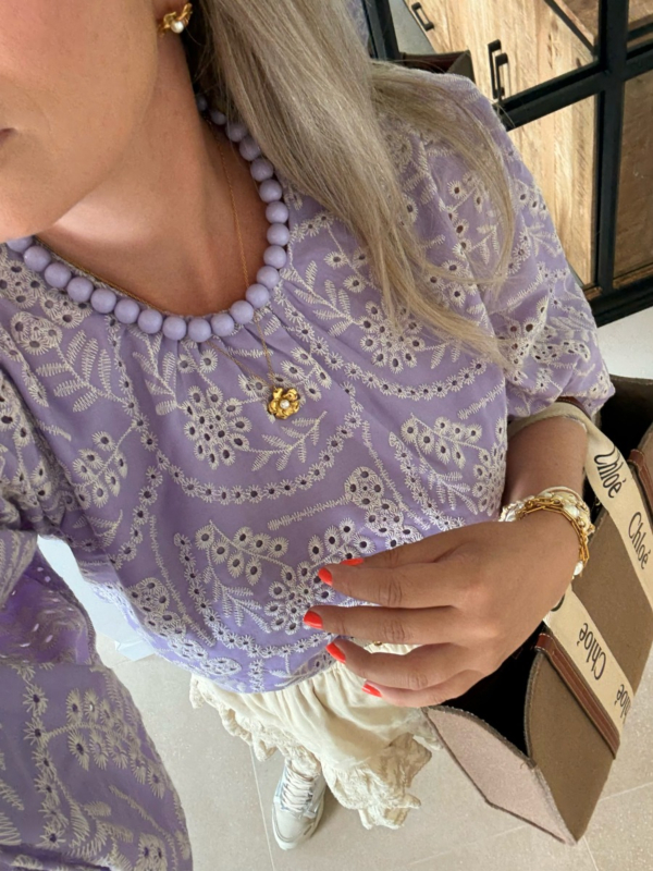 model draagt paarse top met paarse ketting en bloementjes ketting