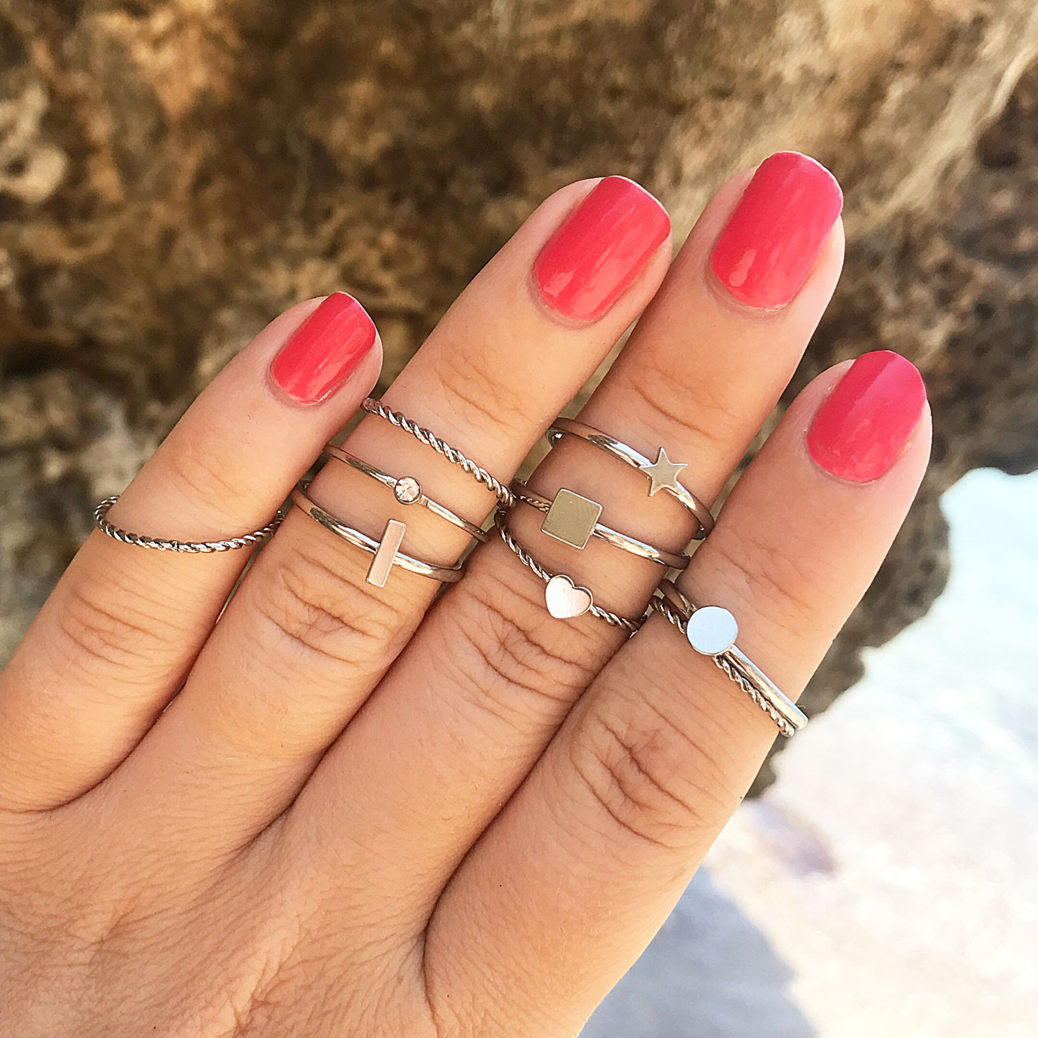 meerdere zilveren ringen om de hand met fel roze nagellak