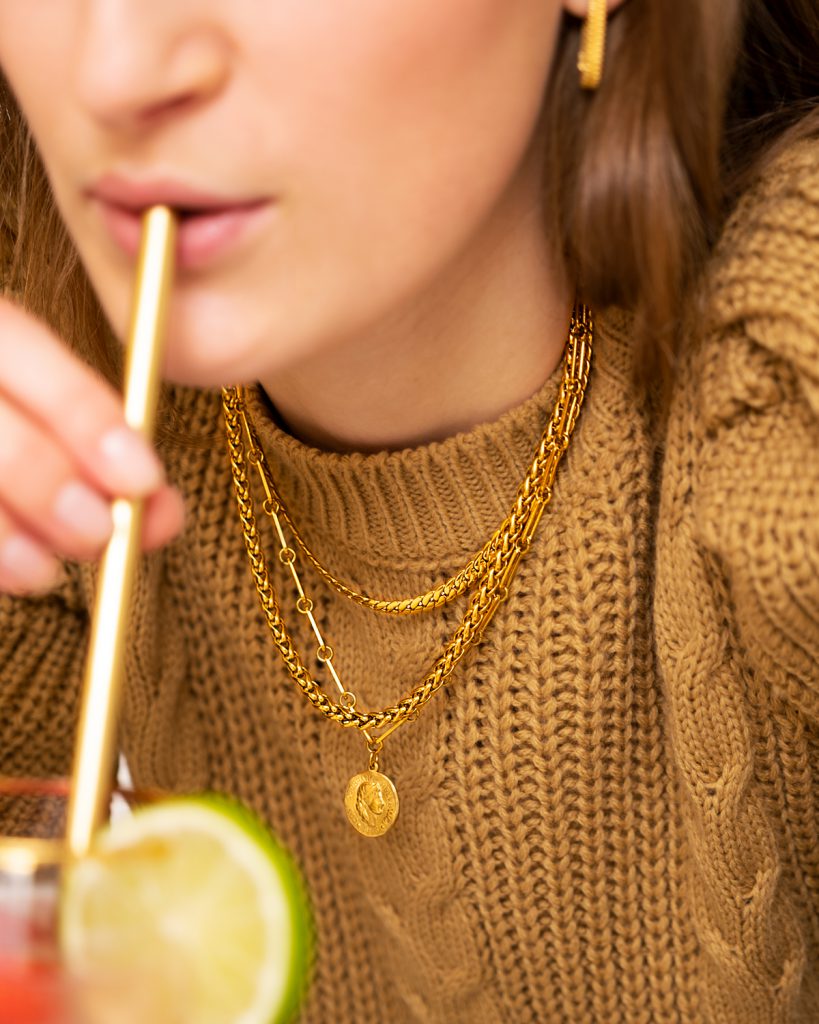 vrouw met gouden kettingen drinkt cocktail