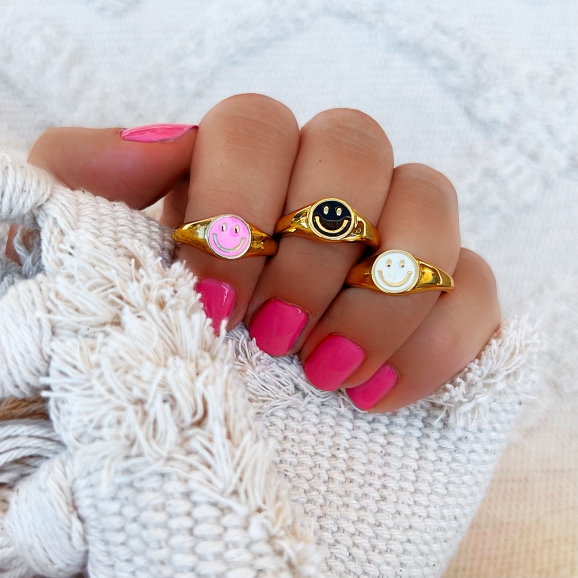 Drie smiley ringen op een hand met roze nagellak