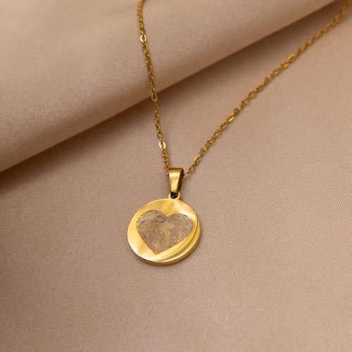 Gouden ketting met rond muntje! In het muntje staat een hartje in de vorm van een vingerafdruk.