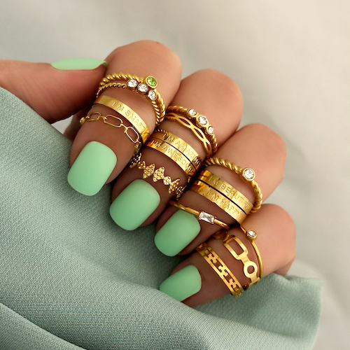Vrouwen hand met licht groene nagels. Ze heeft 16 gouden ringen om haar vingers